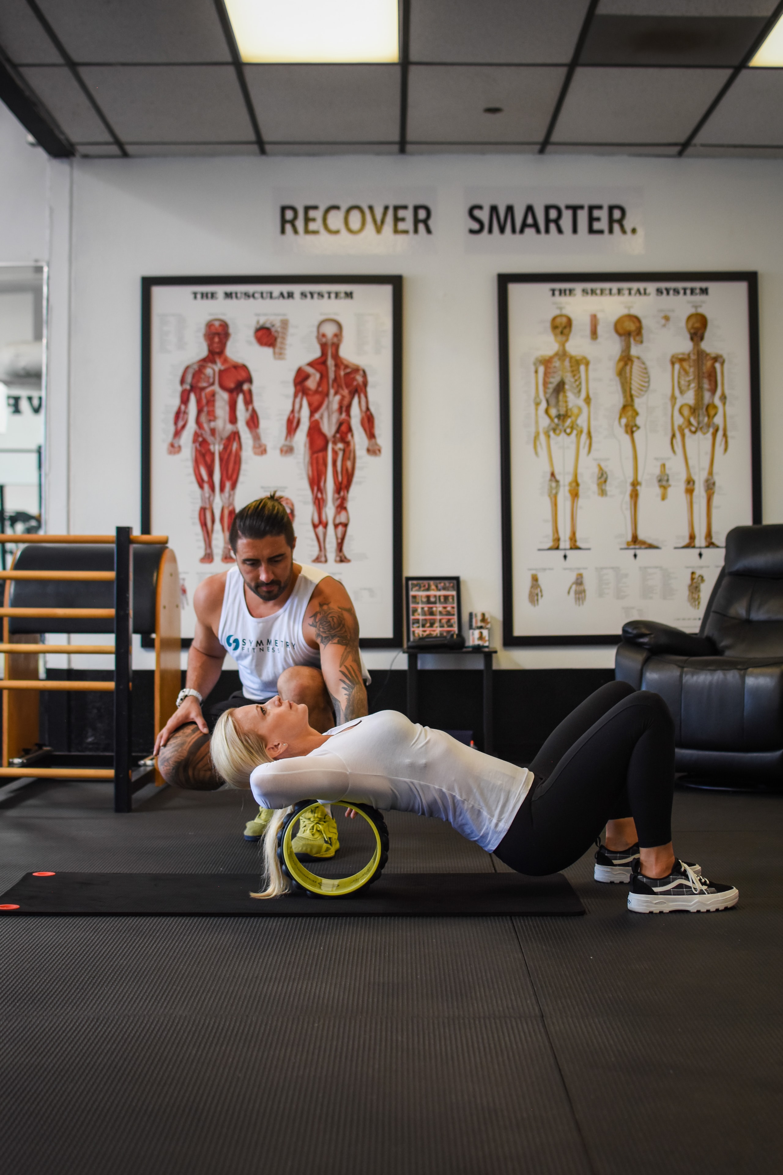 Trainer guiding client through recovery work on a yoga wheel in the Symmetry Fitness studio
